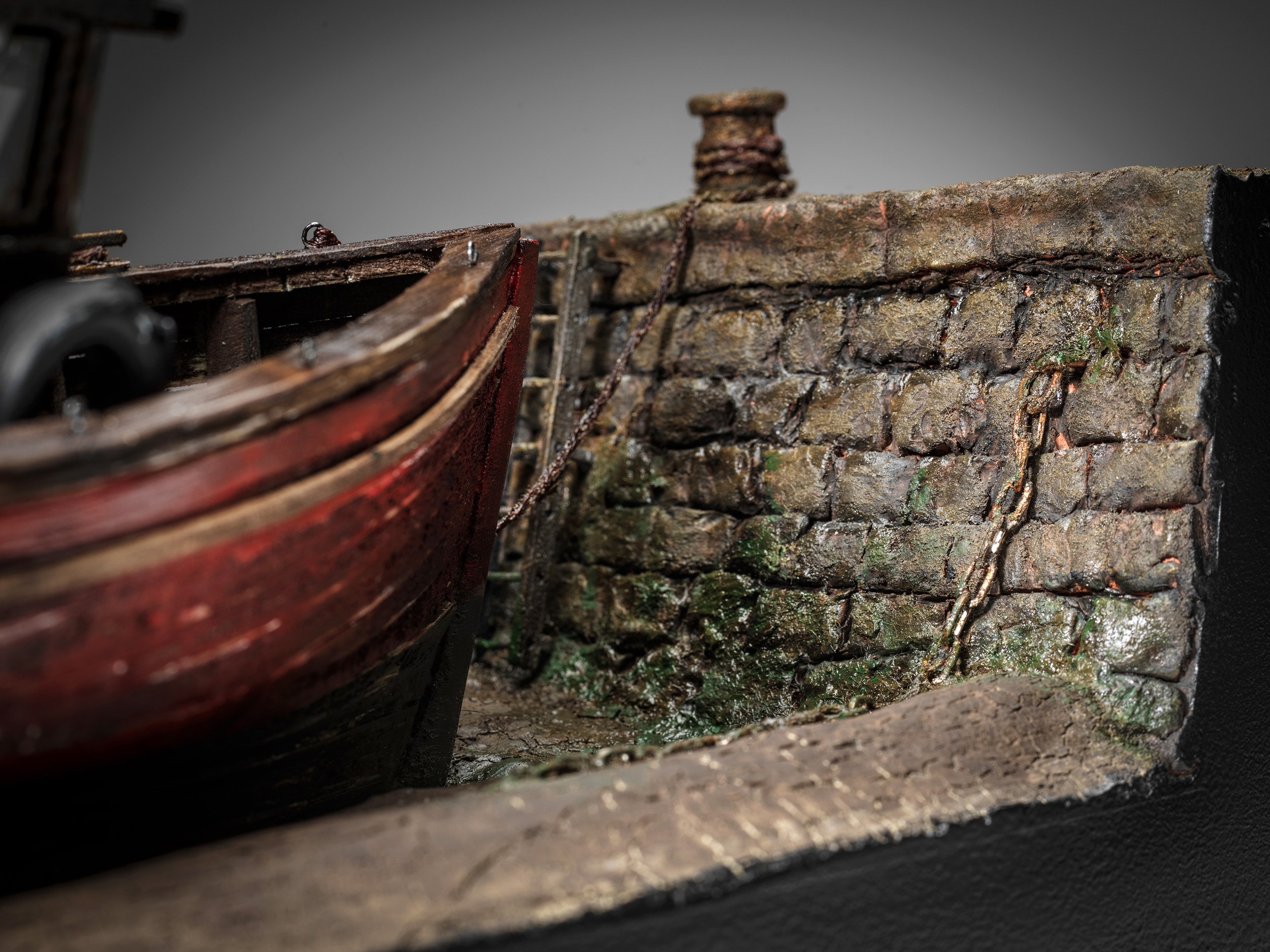 Mollie's bow beside a weathered harbour wall with chain, weed and tidal mud